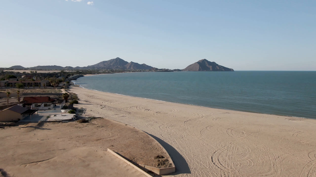 Wide aerial shoreline with beach, ocean, houses, and mountain horizon