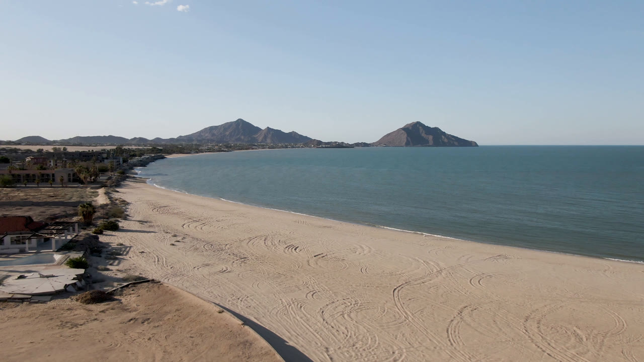 Aerial view of a sandy beach, turquoise water, and distant mountains.