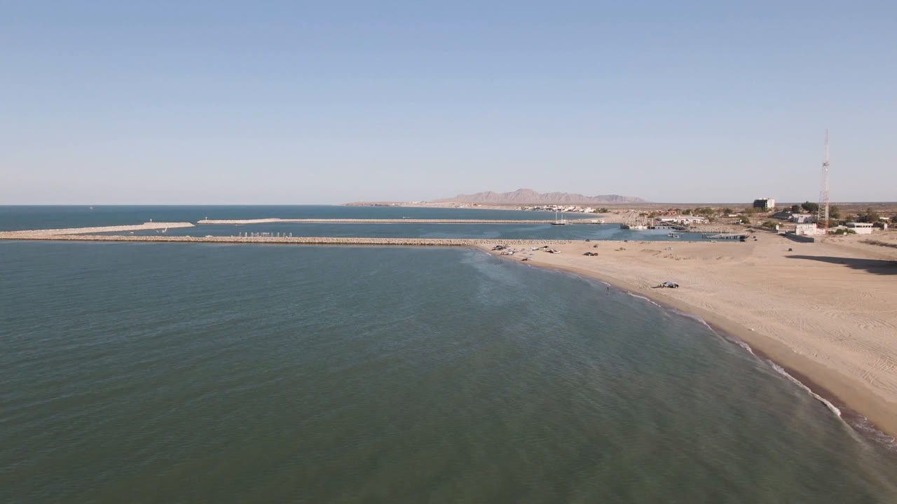 Aerial view in San Felipe, Baja California, Mexico with shallow water filling the foreground, a curved sandy shoreline at right, the pier across the middle distance, and no visible people.