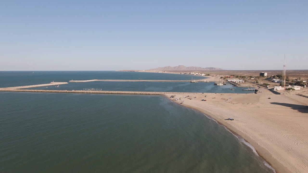 Wide aerial view in San Felipe, Baja California, showing more open water across the lower frame, the sandy shore to the right, the pier spanning the bay, and no visible people.