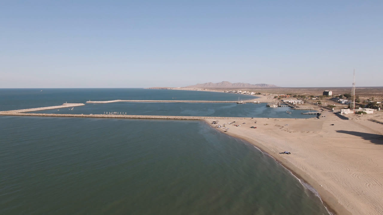 Drone frame of beach shoreline, pier, town edge, and blue water
