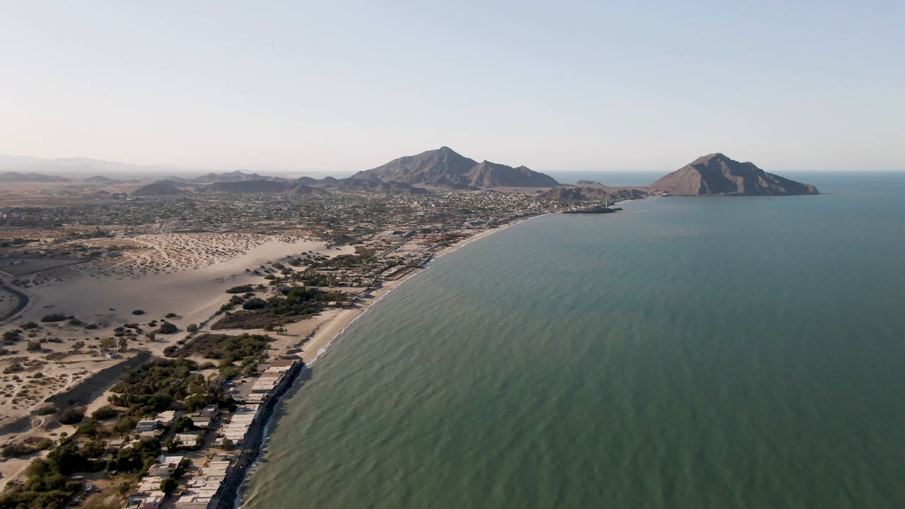 Aerial frame over San Felipe, Baja California, Mexico showing a curving beach beside green-blue water, desert terrain, distant mountains, and no visible people.