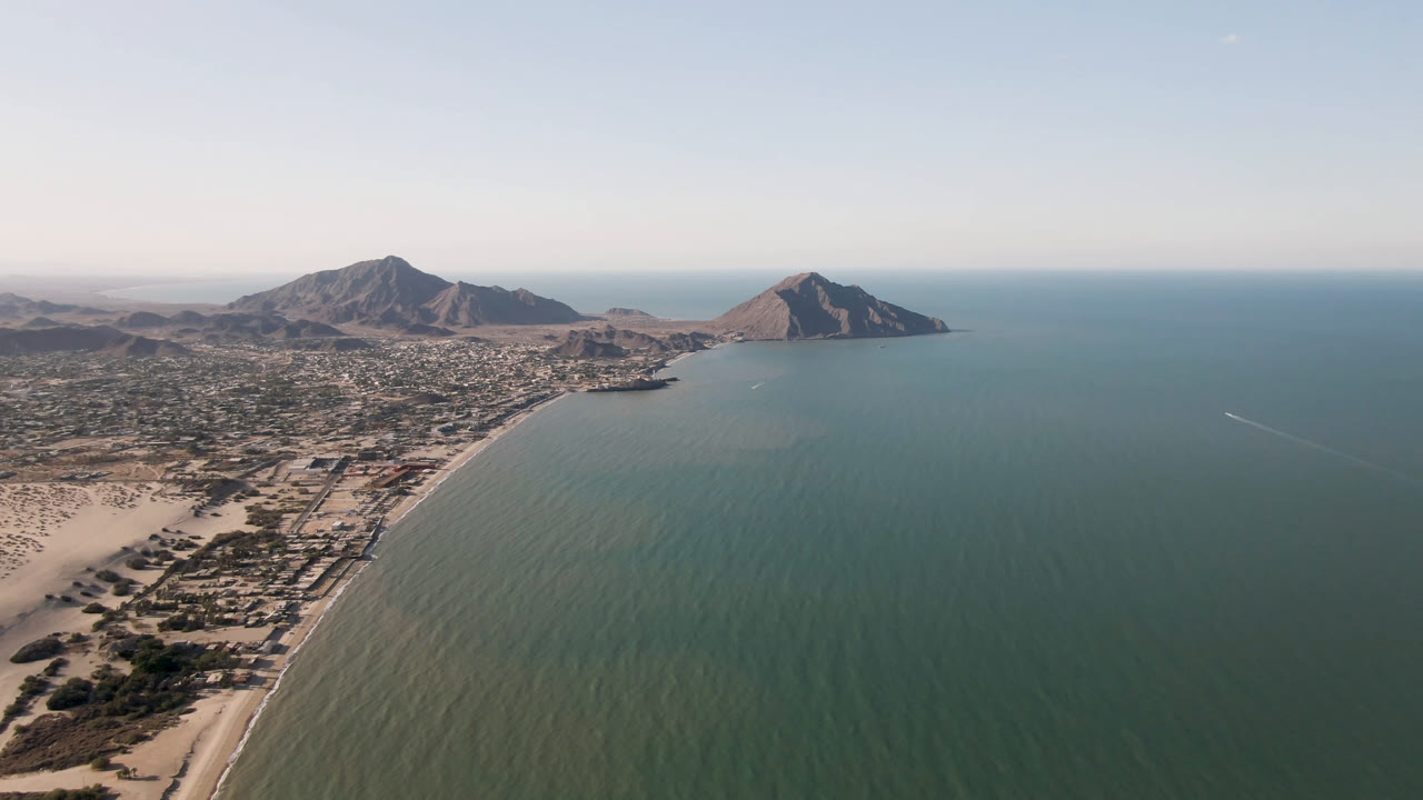 Opening aerial frame over San Felipe, B.C., Mexico, with sandy beach along the left, green-blue water across the bay, mountains on the horizon, and no visible people.