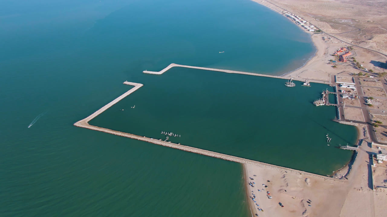 Drone frame of a coastal dock and breakwater system with beach and buildings along the shore.