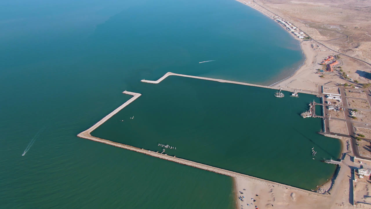 High aerial view in San Felipe BC, Mexico with the dock crossing the lower half of the water, a pale beach at the bottom, inland roads on the right, small boats near shore, and no visible people.