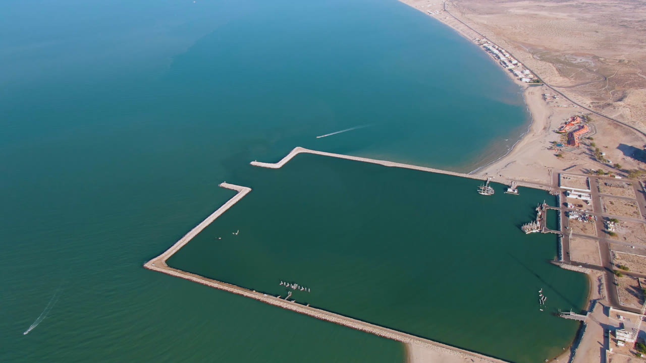 Aerial view in San Felipe, Baja California, Mexico, with the breakwater crossing the center, open teal water below, sandy shoreline above, dock areas on the right, and no visible people.