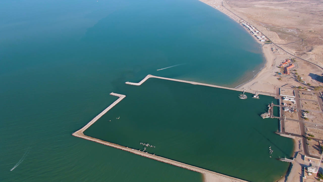 Wide drone view of coastal water, beach, breakwater, and dock area