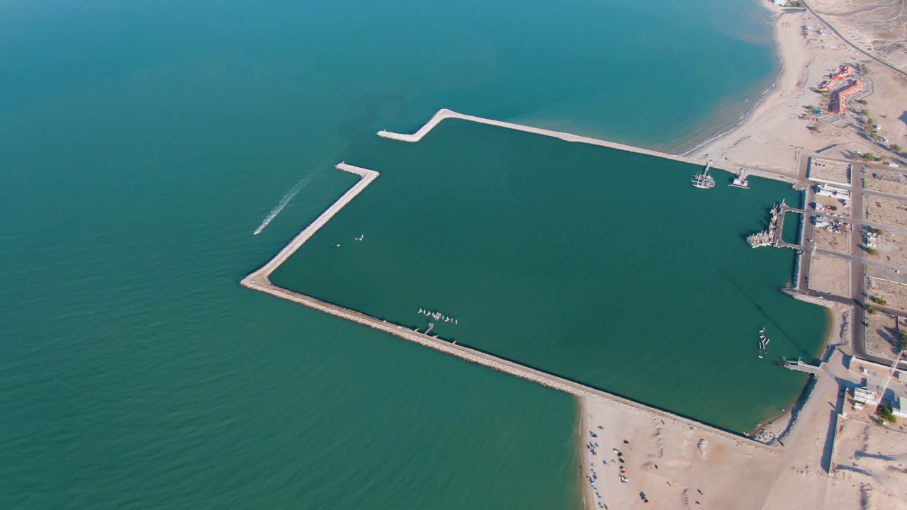 Aerial coastline view with angular breakwaters and sandy land beside the water.