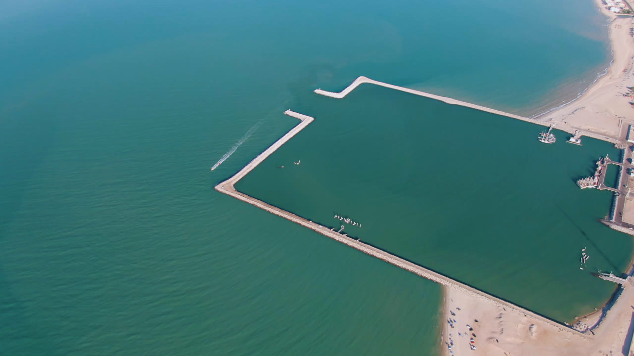 Second frame shows the San Felipe breakwater enclosure centered in turquoise water, with beach and small shoreline structures along the right edge and no visible people.