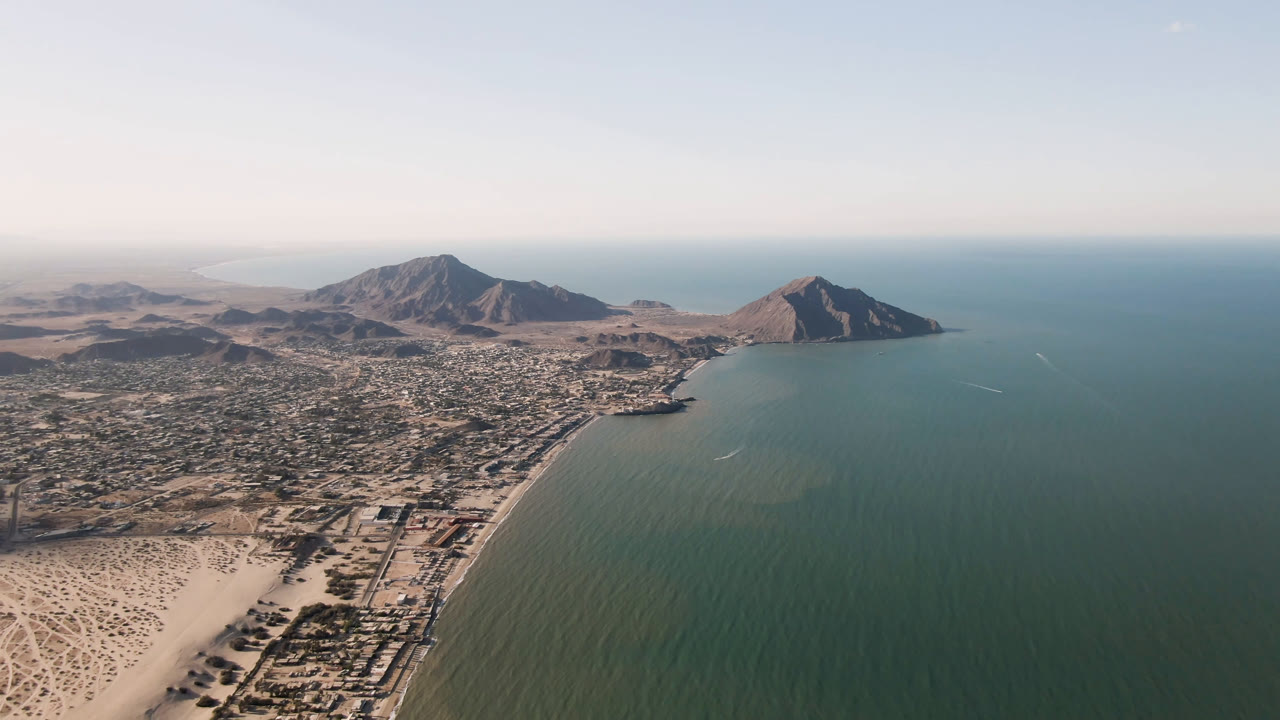 Aerial frame over San Felipe, Mexico, showing the beach and road grid in the lower frame, open bay to the right, distant mountains, light haze, and no visible people.