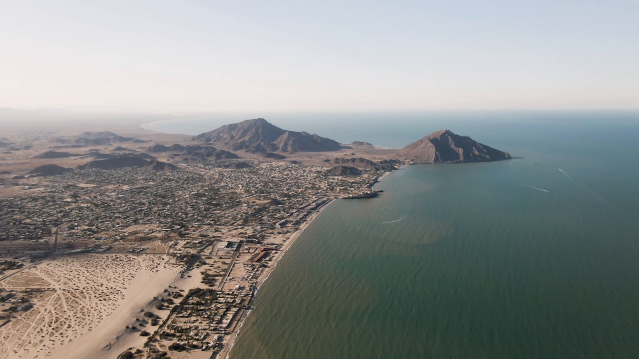 High aerial view of coastal water, sandy beach, town, and mountains