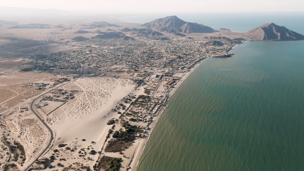 One second into the San Felipe aerial, the frame keeps the shoreline on the right with beach roads and dunes leading into the low town and mountains, with no visible people.