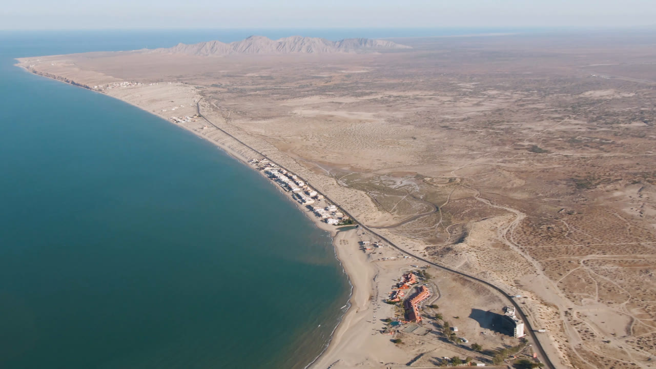 Aerial frame over San Felipe, Baja California, Mexico, with turquoise water on the left, a sandy shoreline and road below, desert terrain beyond, and no visible people.