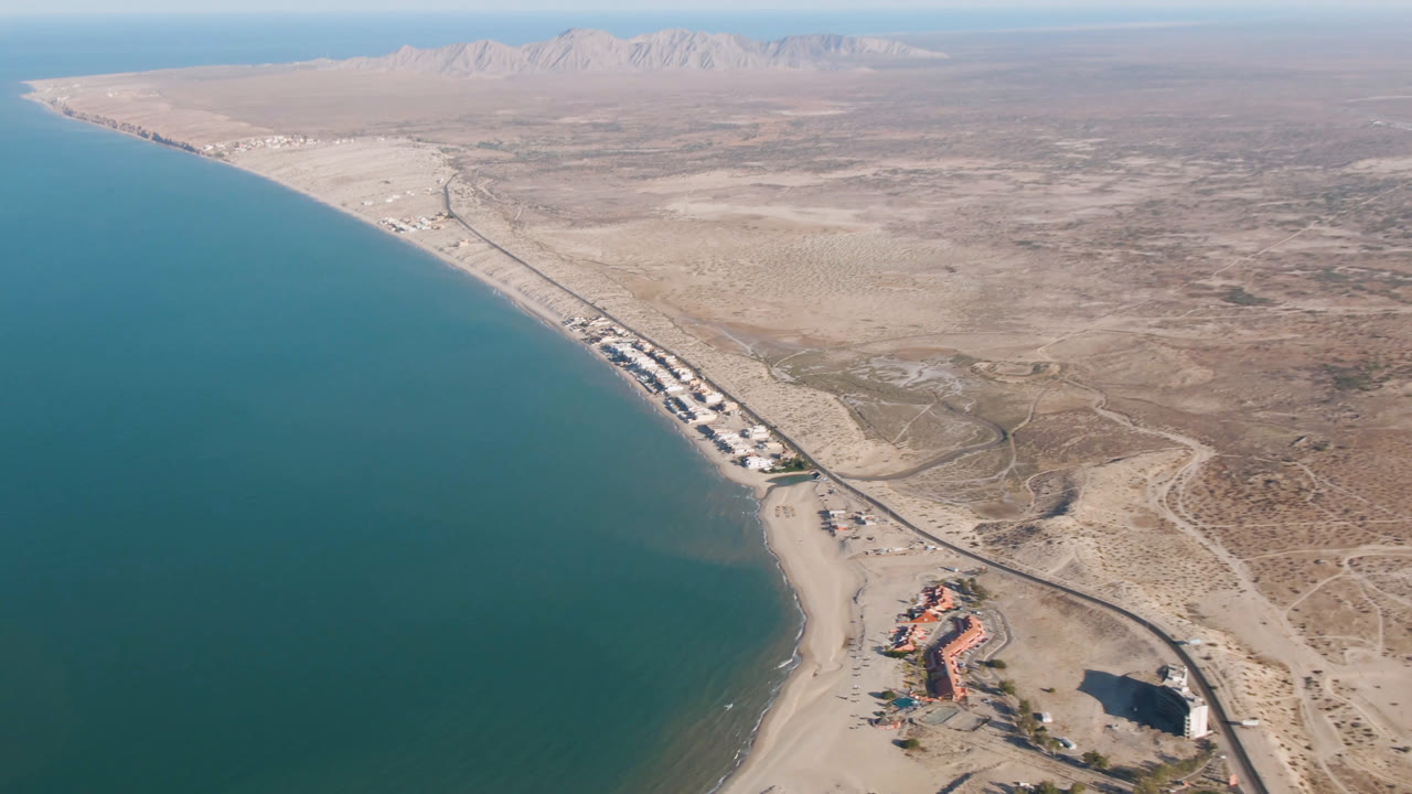Aerial view in San Felipe, Baja California, Mexico, showing the shoreline curving beside teal water, a beachfront cluster near the lower right, desert flats, and no visible people.