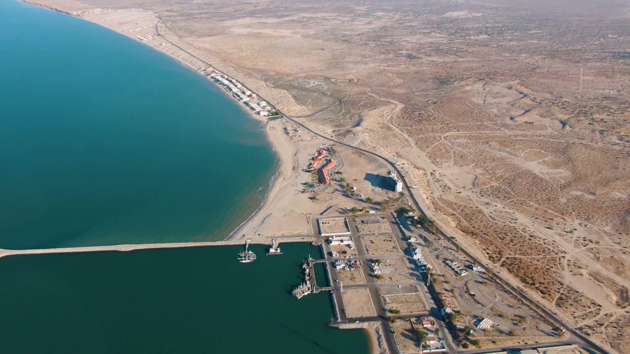 Aerial view of teal water, sandy shoreline, roads, docks, and desert terrain.