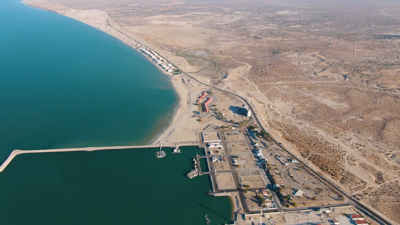 Aerial view over San Felipe, Baja California, with the breakwater extending across the water, docks near shore, a road corridor, and no visible people.
