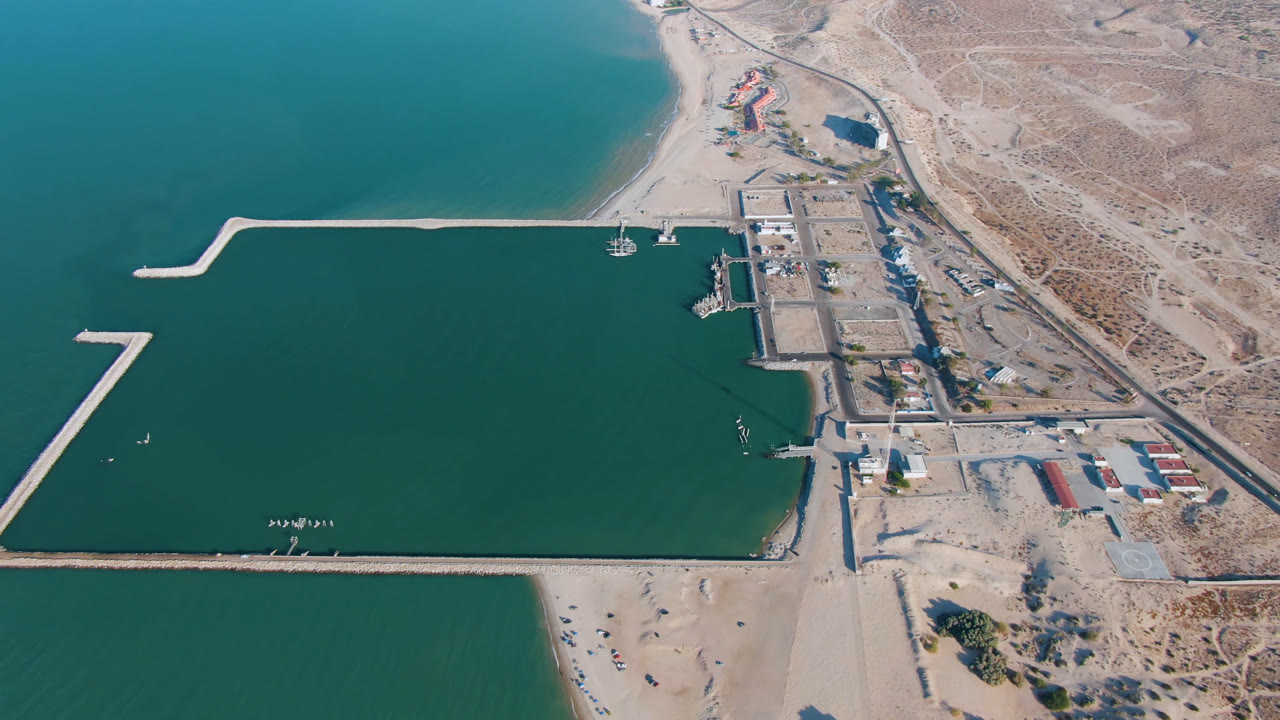 Aerial view over San Felipe, Baja California, Mexico, showing teal water, a sandy beach, long breakwaters, docks, and dry shoreline terrain with no visible people.