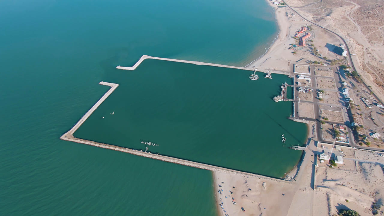 Drone view of open water, marina walls, beach, and dry coastline.