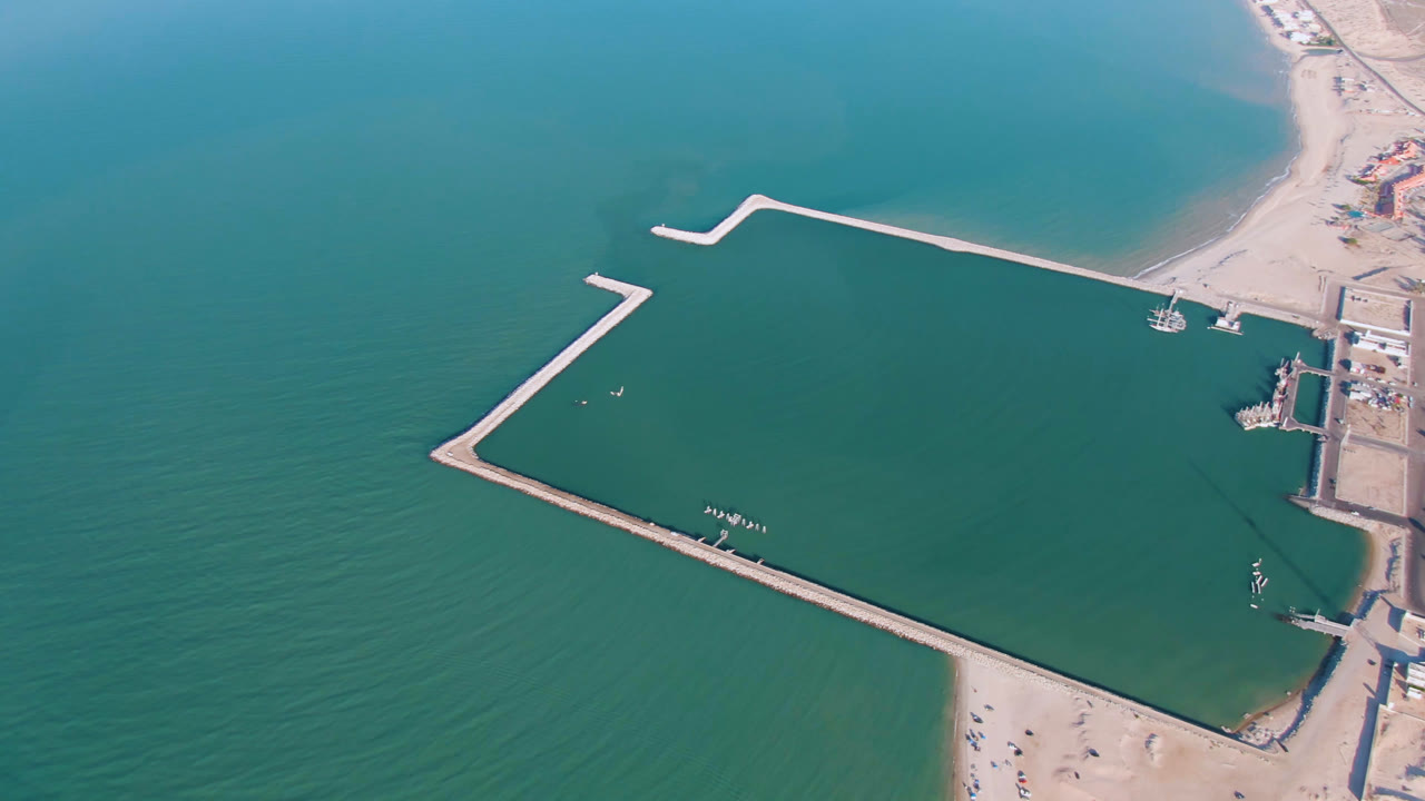 Drone view of beachside harbor basin with docks and breakwaters.