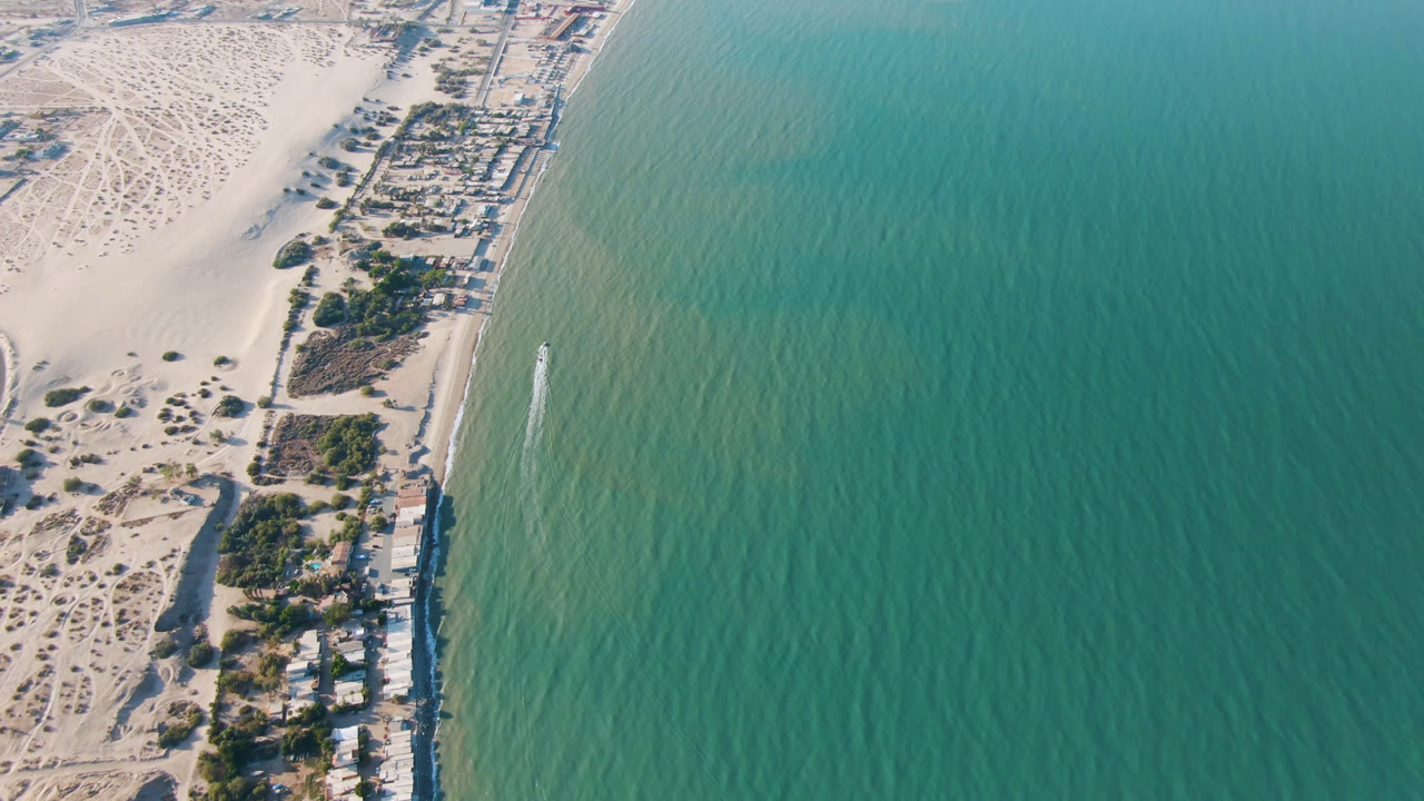 Aerial frame of San Felipe shoreline with beach lots and roads between the pale sand area and the turquoise ocean, with no visible people.