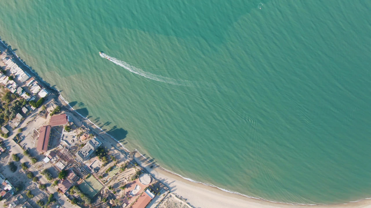 Aerial frame over San Felipe, Mexico with the shoreline angled through the lower-left corner and a small boat cutting across green water with no visible people.