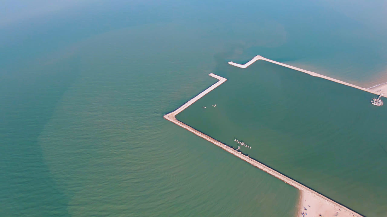 Aerial frame over San Felipe, Mexico, with the pier centered more prominently, calm water on both sides, a small beach edge, and no visible people.