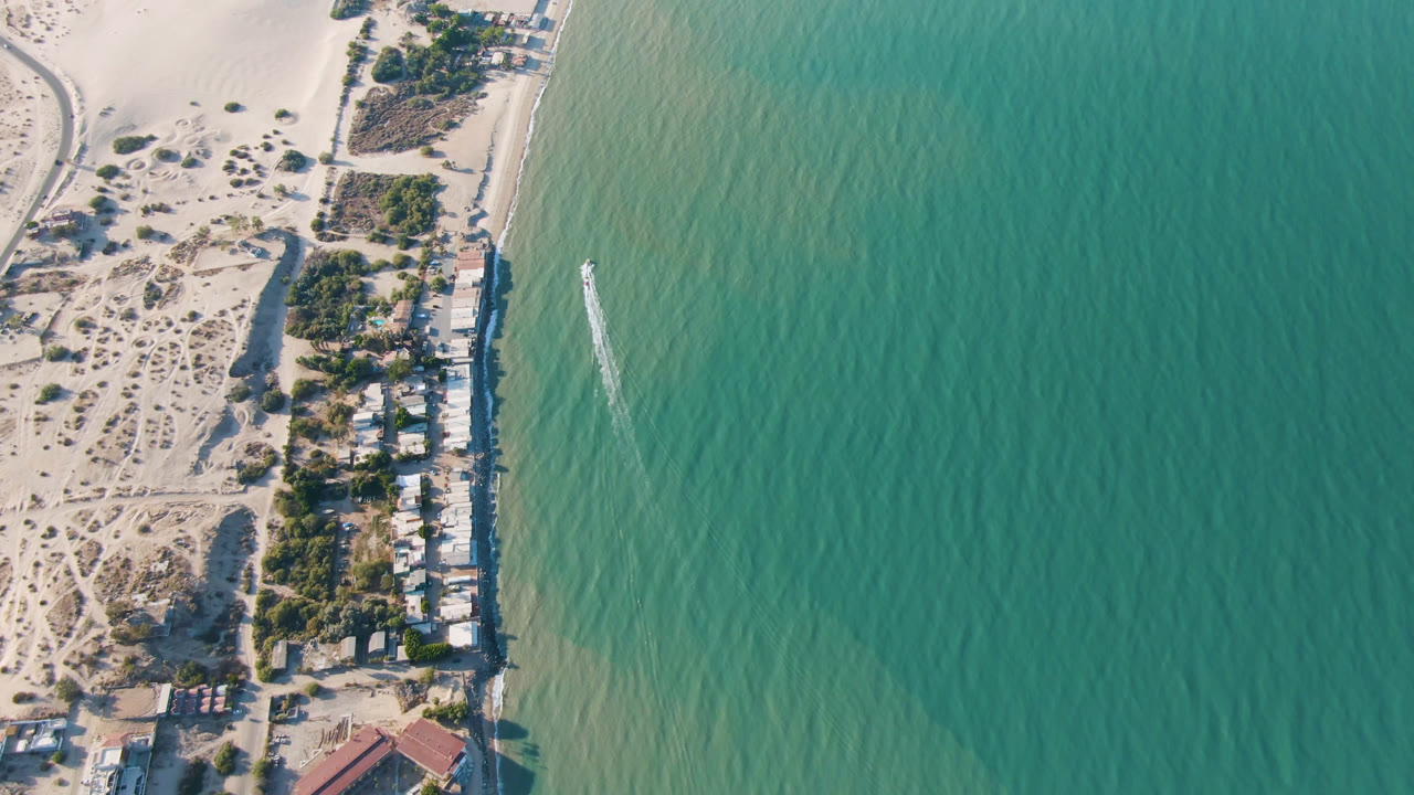 Aerial coastline with beach houses, sand dunes, and open turquoise water.
