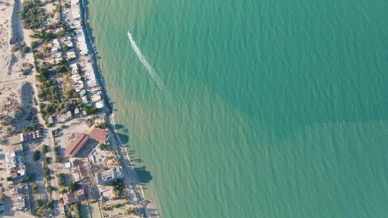 Aerial view in San Felipe, Baja California, Mexico with a thin beach and clustered waterfront structures running between pale sand and green turquoise water, with no visible people.