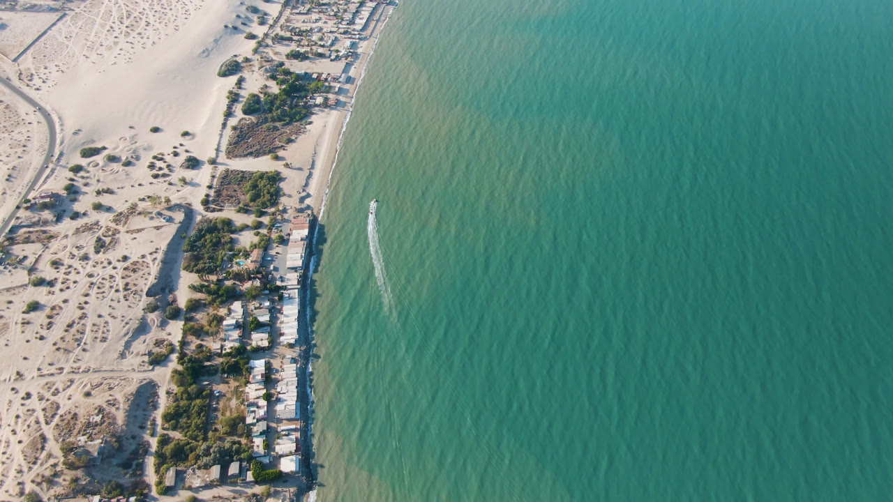 Aerial view of beach houses beside turquoise water and pale sand dunes.