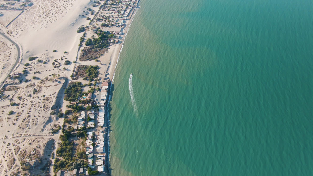 Aerial view over San Felipe, Mexico with the house line running down the beach edge, textured green-blue water to the right, dunes to the left, and no visible people.