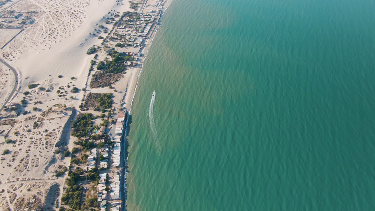 Aerial view over San Felipe, Baja California, Mexico, with pale sand, a line of beach houses, turquoise water, and no visible people at the start of the clip.