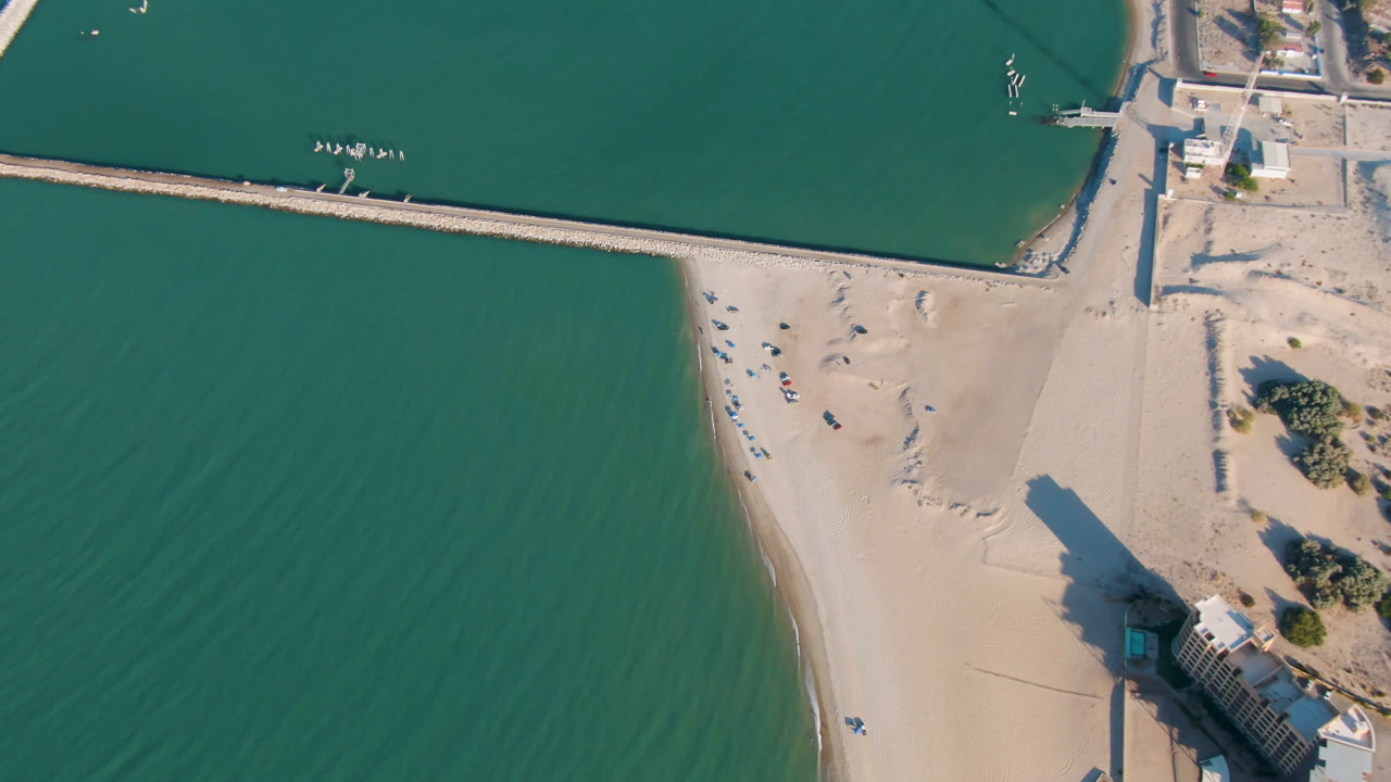 Overhead 2023 San Felipe, Baja California beach frame with green water on the left, pale sand at center, a pier house near the lower right, harbor walls above, and no visible people.