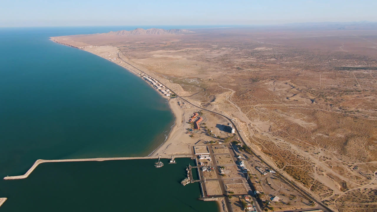 Aerial frame over San Felipe, Mexico with the harbor closer to the lower edge, the sandy beach curving along the water, arid land spreading inland, and no visible people.