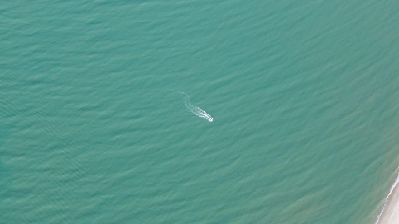 Overhead view of a small white boat on turquoise water near the right-side beach edge in San Felipe BC, Mexico, with no visible people.