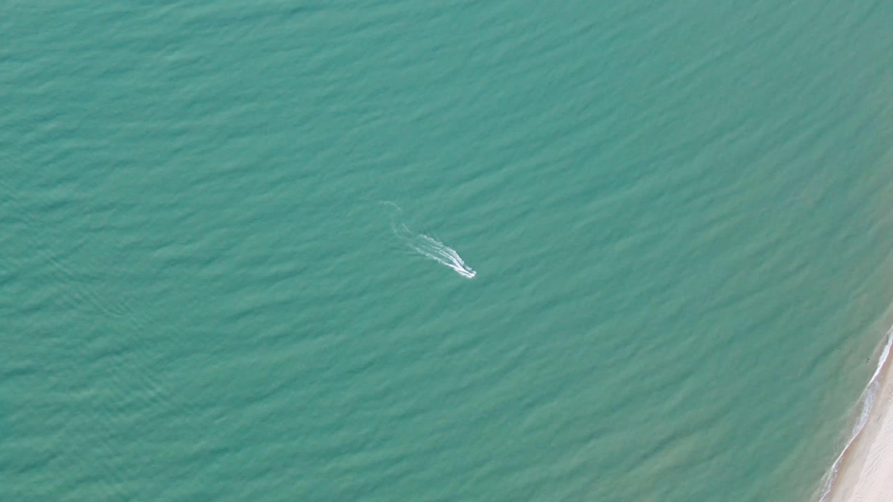 Small boat on open turquoise water beside a sliver of beach.