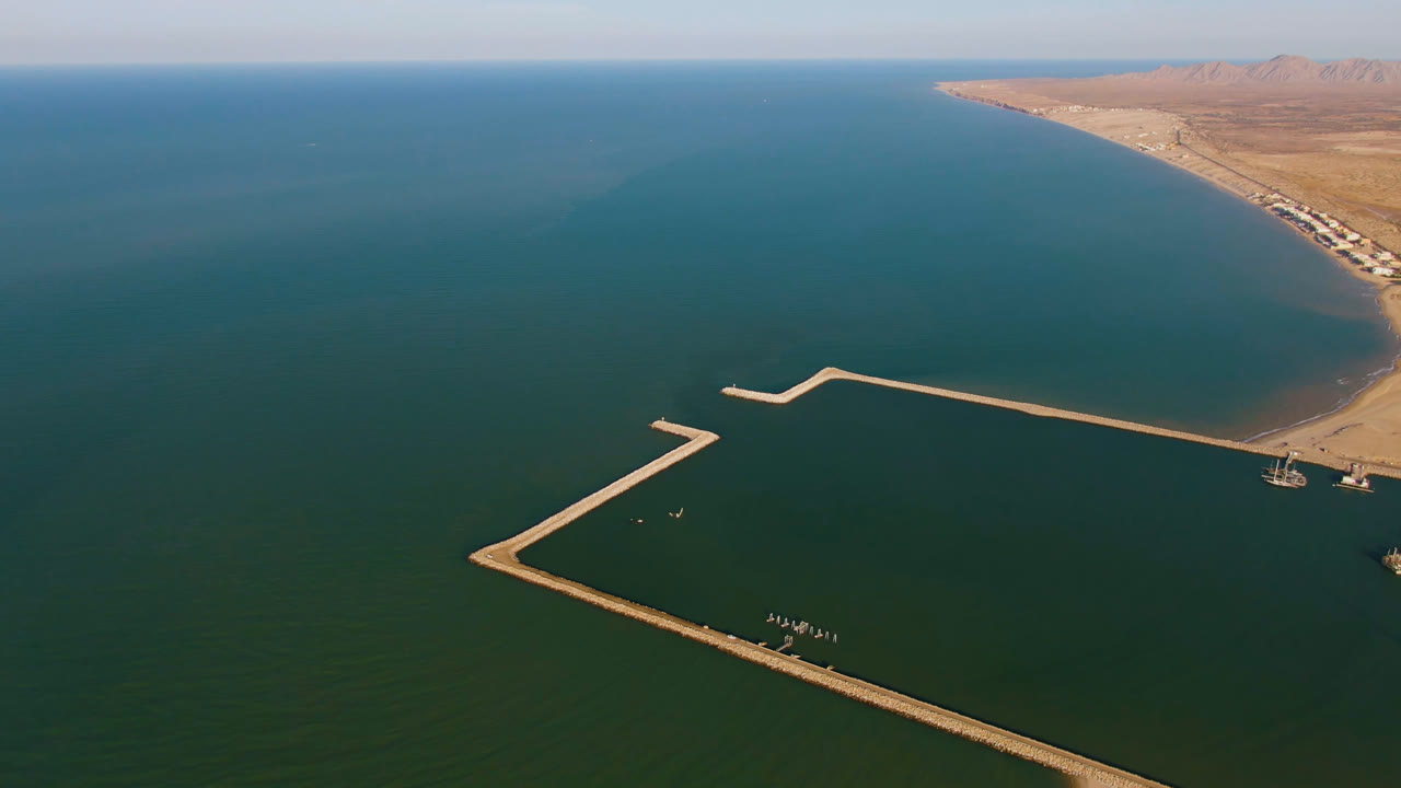 Second frame holds a high drone view over the San Felipe marina, with the long dock crossing the water, small watercraft near the breakwater, and no visible people.