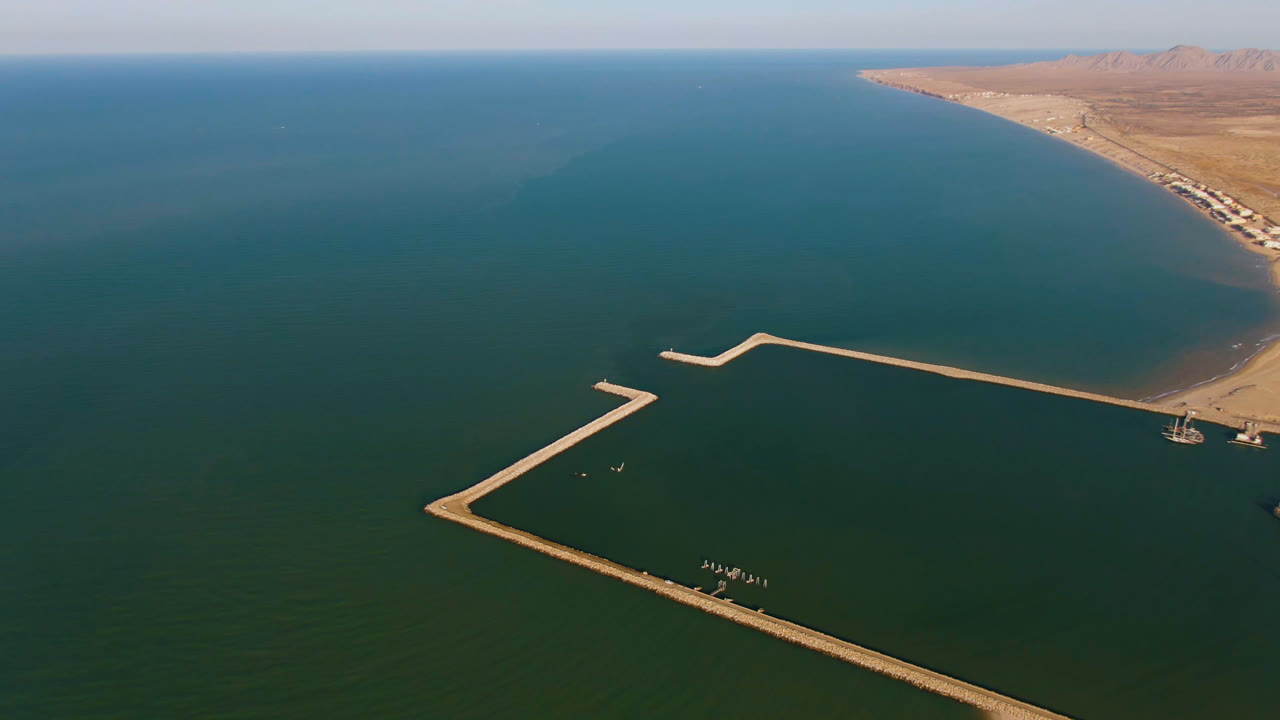 Aerial coastal view with a long dock, green-blue water, and shoreline at the upper right.