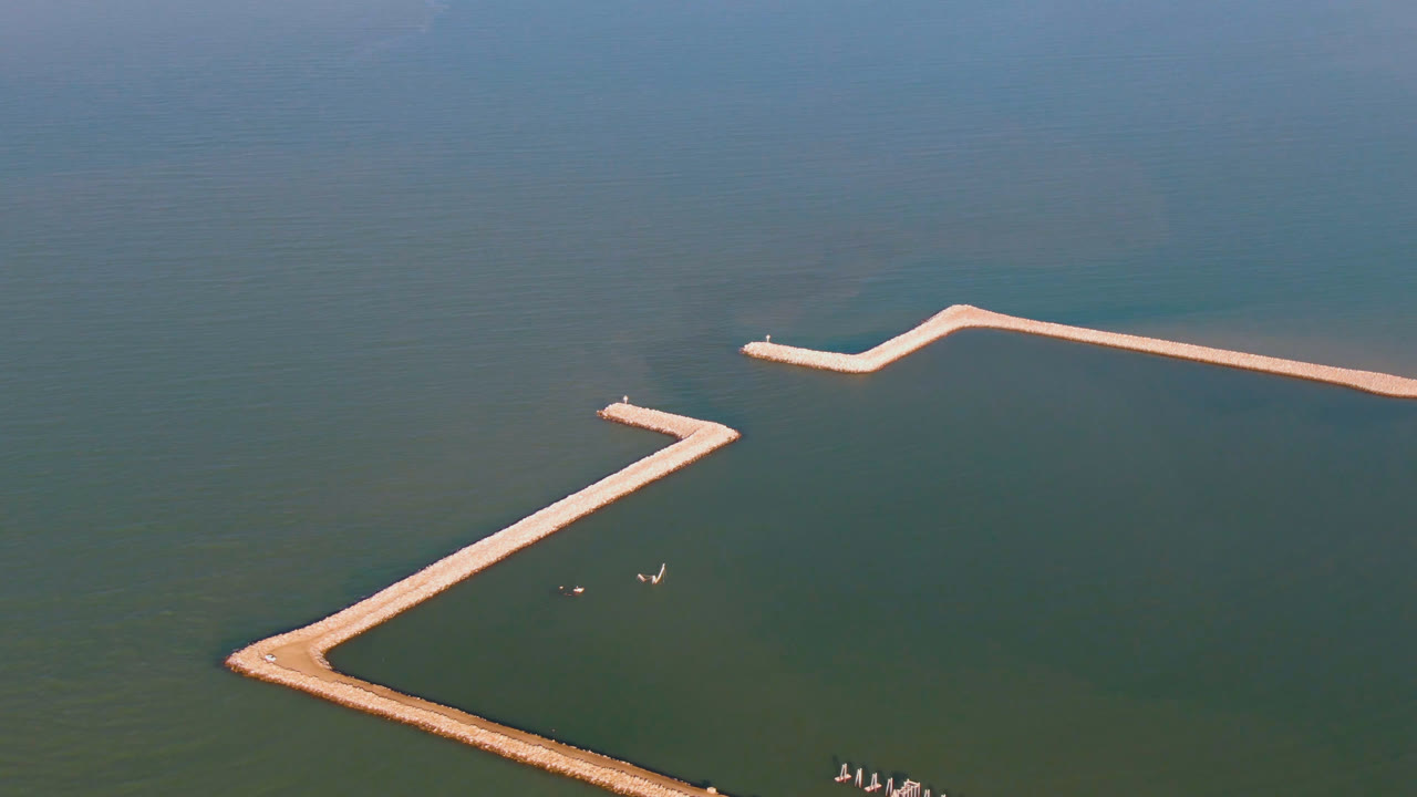 High aerial frame over San Felipe coastal water with a pale zigzag dock or breakwater cutting across green-blue water and no visible people.