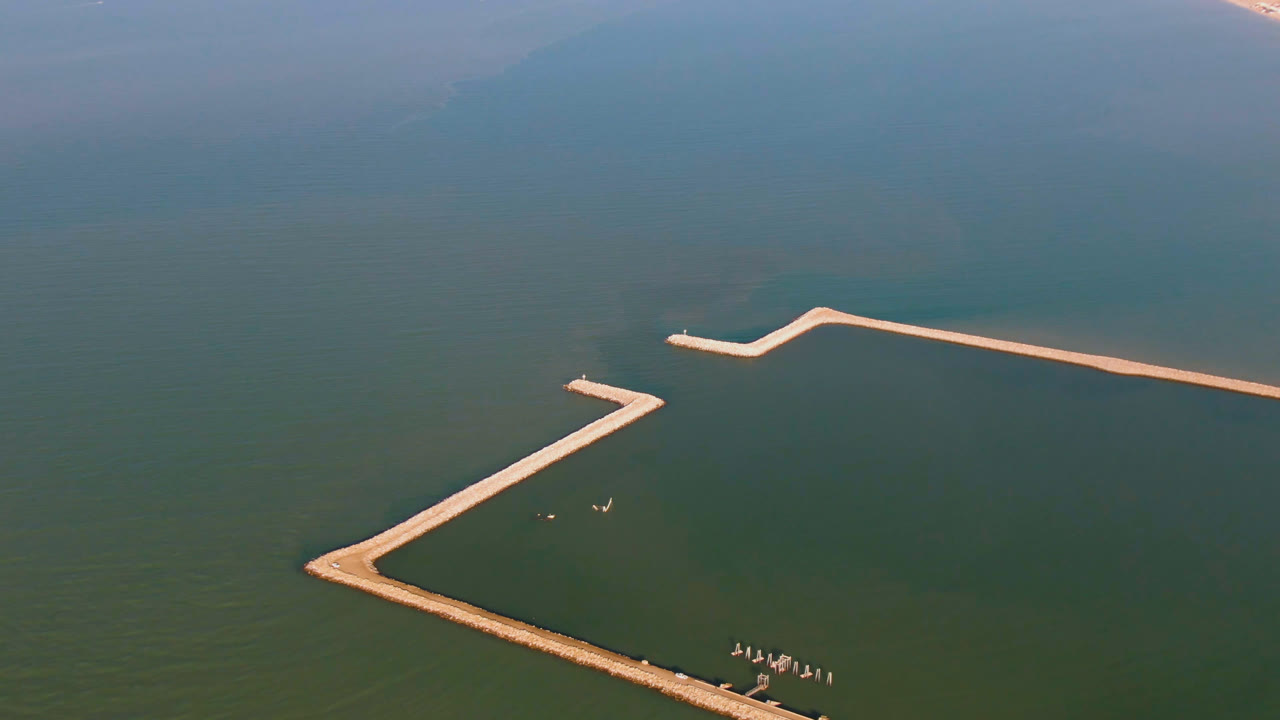 Aerial view in San Felipe, Baja California, Mexico, with a long pale pier stretching across the upper water and an angled pier entering from the lower edge, no visible people.