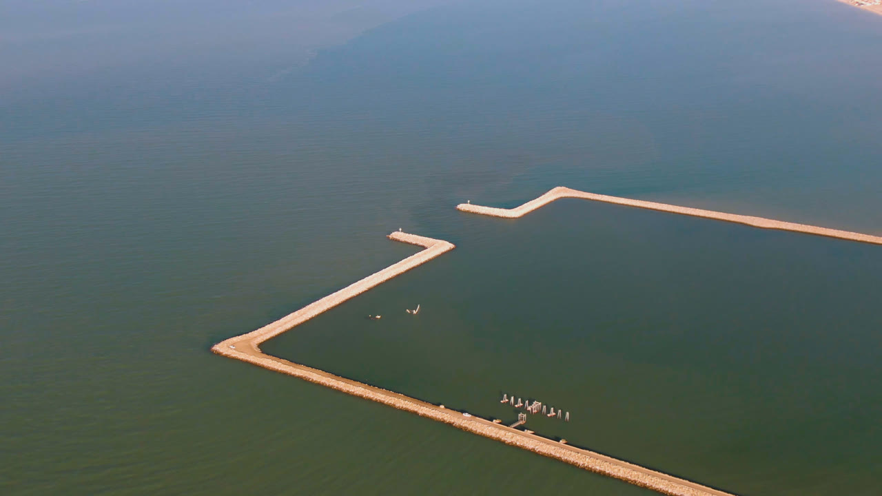 Aerial frame over San Felipe, Baja California, Mexico, showing an angular pale dock crossing green-blue water with distant shoreline and no visible people.
