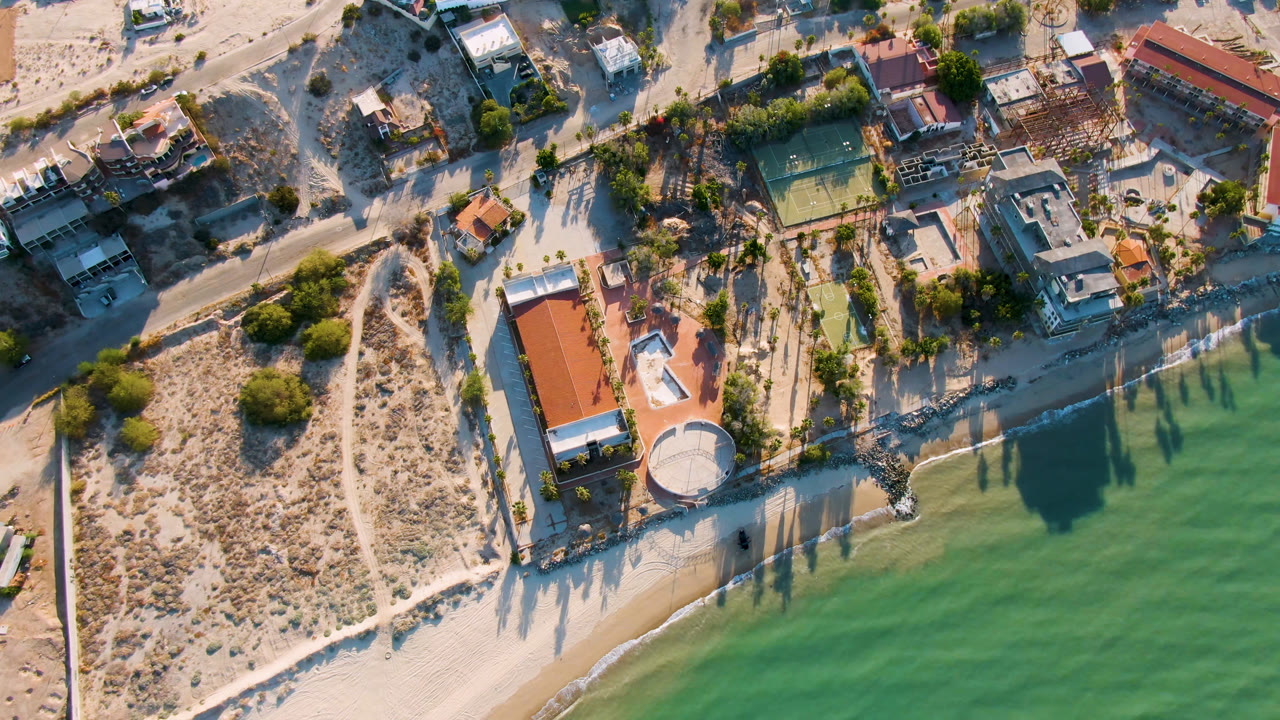 Aerial view in San Felipe BC, Mexico holds over the beachfront house and circular structure, with the tennis court and neighboring homes inland and no visible people.