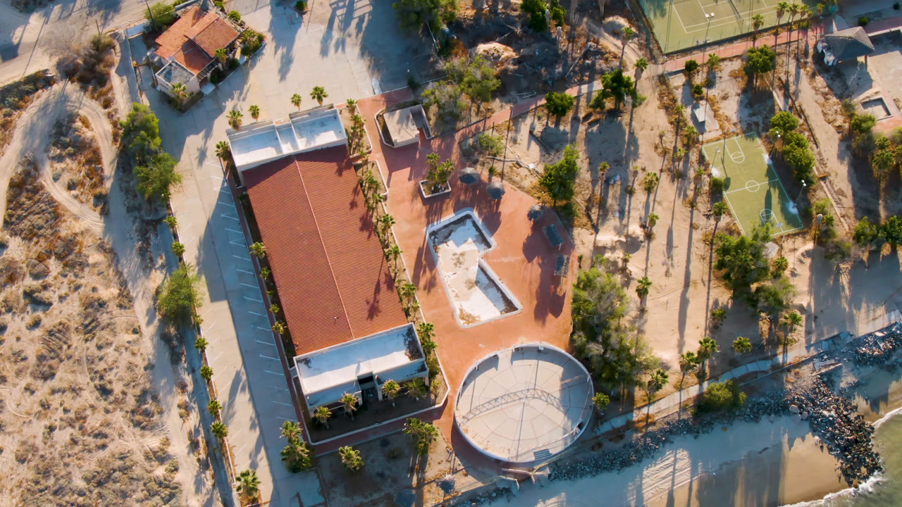 Overhead view of a red-roofed house near water and a tennis court.