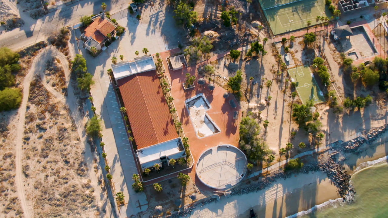 Drone view of sandy paths, house, tennis court, and green shoreline
