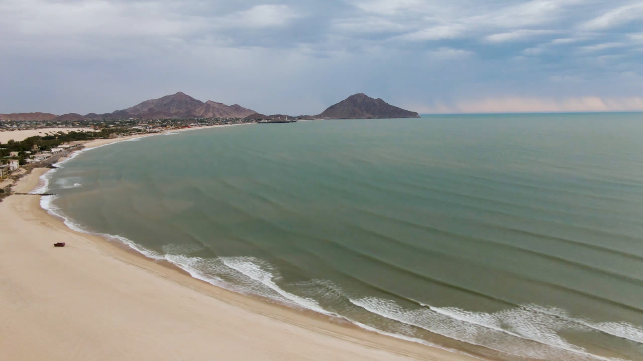Aerial view of a sandy beach, green-blue water, and distant mountains.