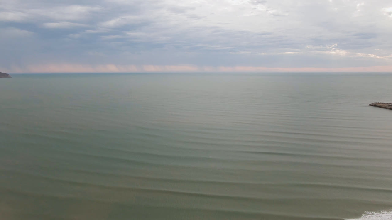 Aerial view over muted green water near San Felipe, BC, Mexico, with rippled ocean in the foreground, gray clouds above the horizon, distant land at both edges, and no visible people.