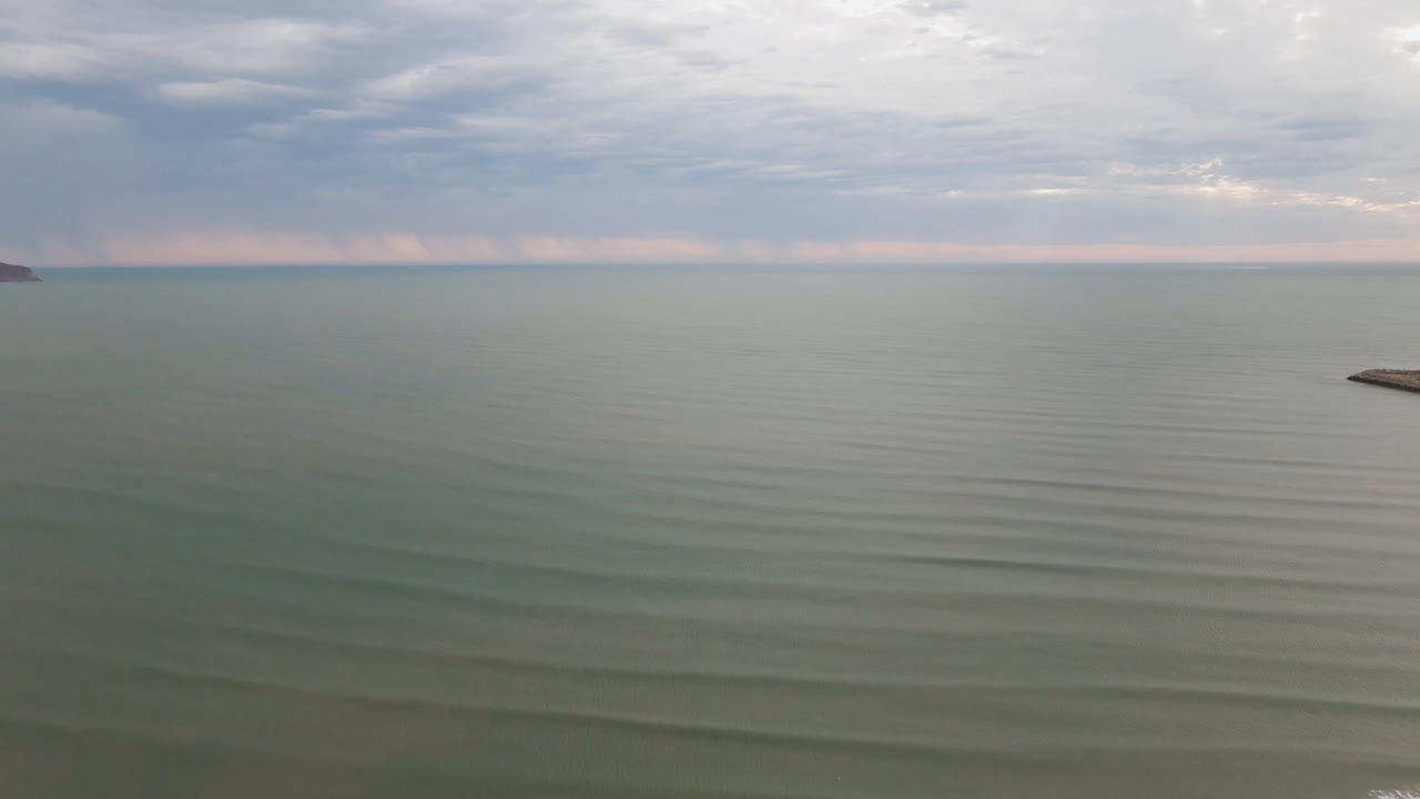 Aerial frame from San Felipe, BC, Mexico, showing broad calm water, a high cloudy horizon, a small shoreline or breakwater point near the right edge, and no visible people.