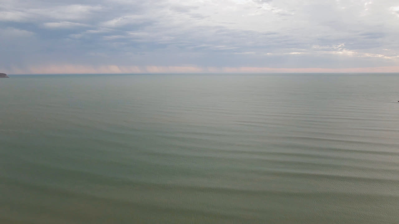 Wide aerial view of calm green-blue water in San Felipe, BC, Mexico, with a cloudy horizon, faint ripples, and no visible people.