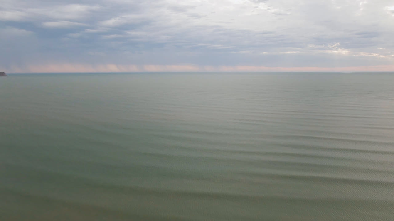 Aerial frame over San Felipe water with a tiny dark boat or object near the distant horizon, layered clouds, and no visible people.