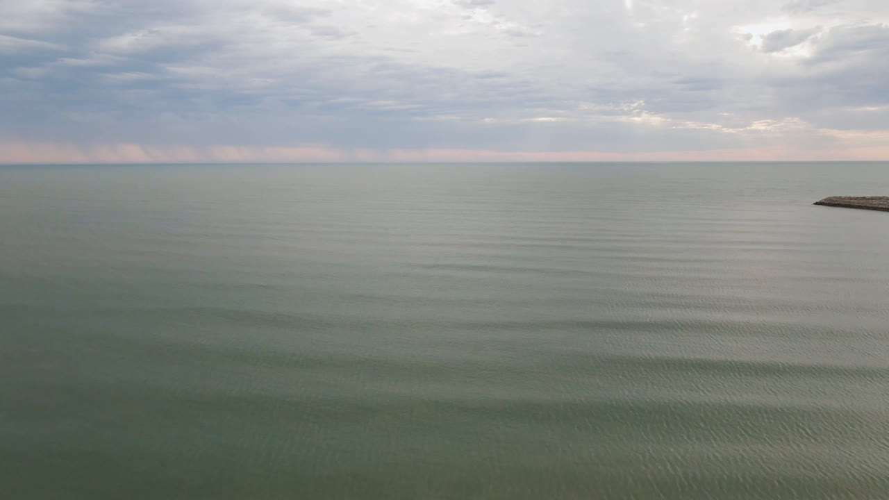 At 0:01 in San Felipe, B.C., Mexico, the ocean remains still under layered clouds while a small rocky breakwater enters at the right edge, with no visible people.