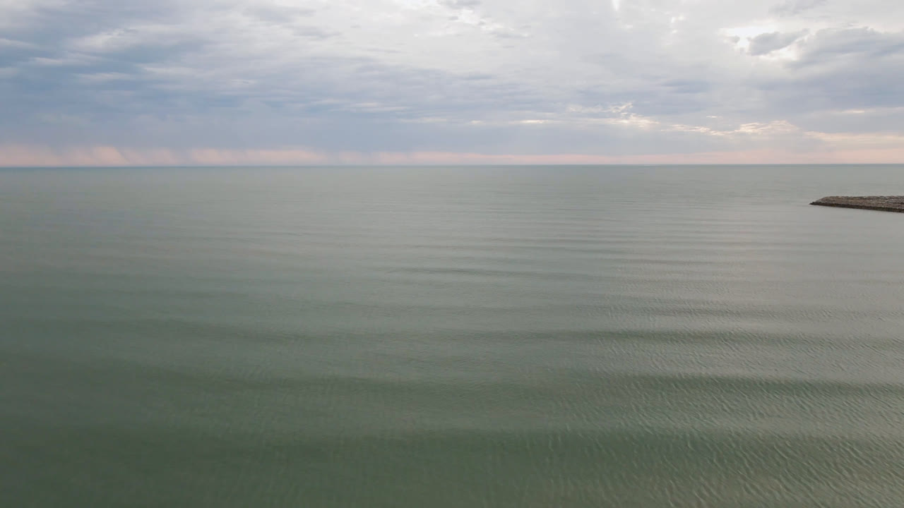 Minimal ocean view with cloudy sky and rocky breakwater at right